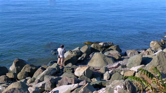 Man observing sea wide shot from a rocky shoreline, showing coastal recreation and nature watching for travel, tourism, outdoor leisure, waterfront visits and shoreline destination coverage