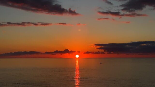 Sun setting over sea, wide view of a glowing horizon with dark clouds and orange reflection on water, suited for travel, weather, meditation, nature, background and commercial media projects