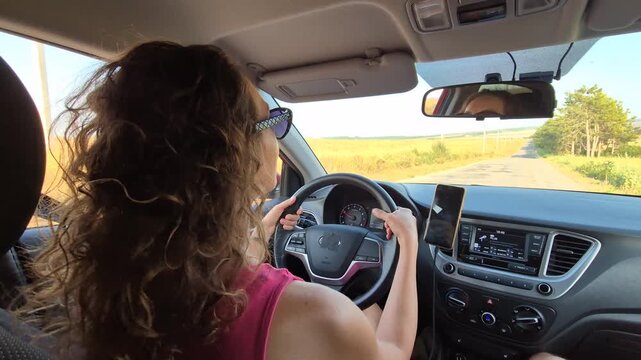Woman driving car, road travel concept, happy female traveler journey, sunset countryside highway. Interior dashboard camera view, front seat side shot.