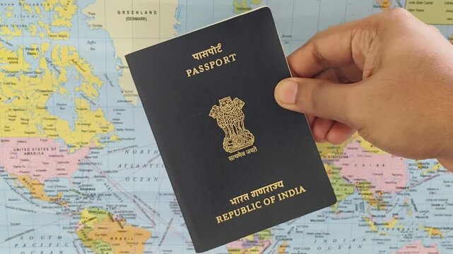 Indian passport tourist or student holding in hand with blurry world map background. International travel, foreign trip, study abroad, overseas education or global migration concept. Closeup side view