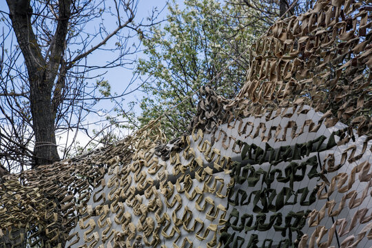 Military camouflage net stretched outdoors against spring trees