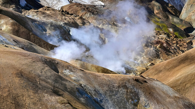 Billowing geothermal steam rises from colorful volcanic slopes with lingering snow near Kerlingarfjoll in the Icelandic highlands.