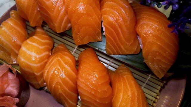 Fresh salmon sushi pieces arranged tightly on round serving plate with bamboo mat liner, glossy orange fish, leaf garnish, soft marble table backdrop, premium dining presentation