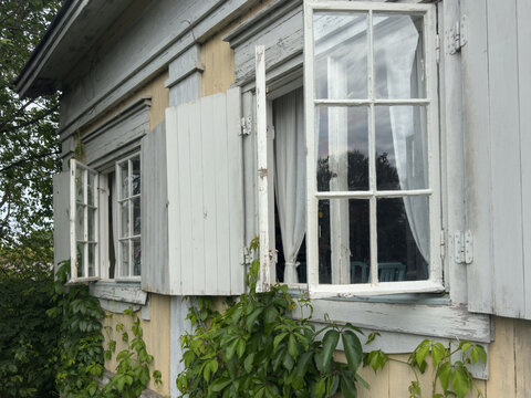 Open casement windows and weathered wooden shutters surrounded by climbing greenery on a traditional house at Suomenlinna sea fortress in Helsinki, Finland.