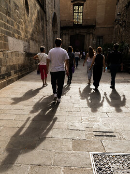 Spain, Barcelona. People walking towards dark doorway on stone paved alley.