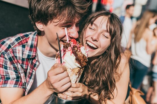 Young couple laughing while sharing a large decadent ice cream sundae on a sunny summer afternoon
