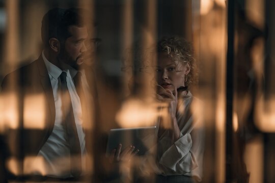 Business colleagues discussing a project on a digital tablet inside a dark modern office building