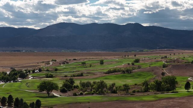 Aerial of golf course in Lakewood Colorado with mountain range and cloudy sky with manicured fairways and cart paths in summer