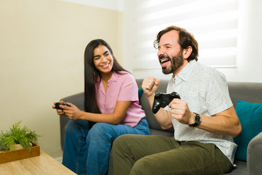 Fun couple enjoying leisure time playing video games on the couch at home, celebrating a winning moment