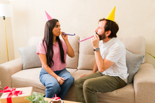 Young man and woman sitting on a couch, having fun at a birthday celebration with party hats and blowouts