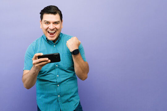 Excited man celebrating victory while playing mobile game on smartphone, winning and achieving success