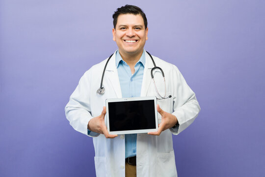 Medical doctor smiling, presenting a digital tablet with blank screen, showcasing healthcare technology and online medical services