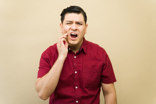 Hispanic man experiencing severe toothache, touching cheek, suffering from oral discomfort and dental pain