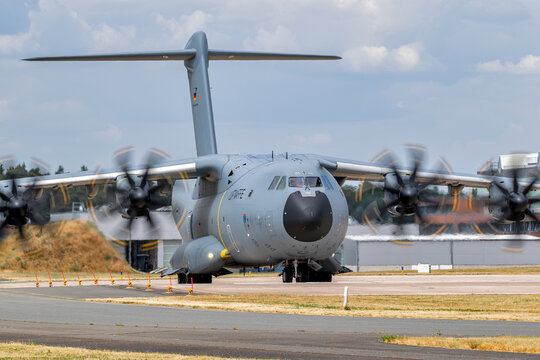 Airbus A400M tactical transport aircraft taxiing with motion-blurred turboprop propellers.
