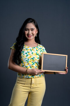 Portrait of young woman holding a blank blackboard in yellow theme cloth