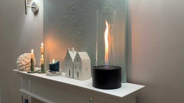 Horizontal 4K video showing a static side angle view of a modern black bioethanol fireplace with a burning flame on a white wooden mantel. 