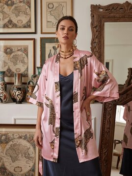 Stylish woman wearing a pink silk kimono robe with a leopard print pattern and a dark slip dress in an art-filled room.