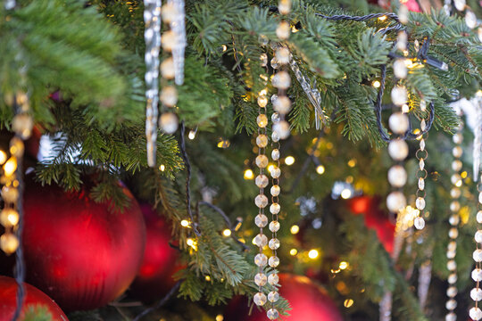Pine branches with crystal beads and red baubles. Warm golden bokeh lights. Christmas tree decoration close-up. Background for New Year's or Christmas greetings. Festive winter atmosphere. Copy space
