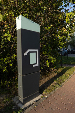 Parking exit sign. Black sign with white arrow indicating exit from parking area. Foliage in background