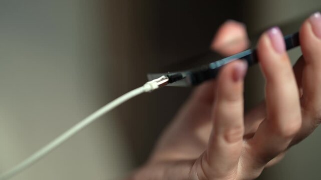 Female hand with manicure inserting power cord into modern smartphone to charge battery. Concept of connection between technology and daily life, close-up, slow motion. Concept of modern technology.