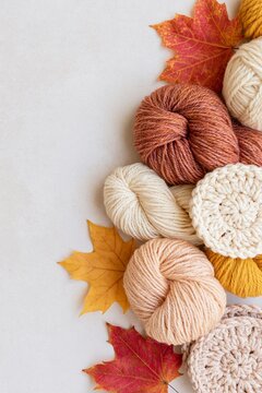 Autumn knitting composition with warm wool yarn, crochet pieces and colorful maple leaves arranged along the edge with generous copy space
