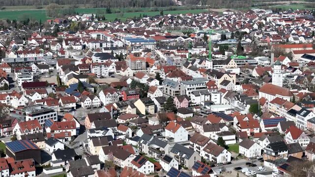 bavarian town rooftops illertissen aerial view church spire distant construction crane red tile roofs solar panels residential streets farmland treeline rural germany drone footage travel destination