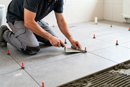 Tiler laying large grey floor tiles in a bathroom, bathroom renovation
