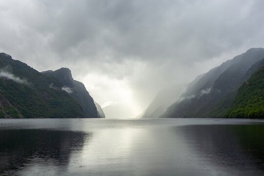 Fjord landscape with dramatic cloudy sky, rain, and light breaking through the mist