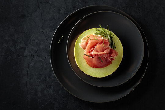 Italian prosciutto with melon and fresh rosemary on a black background.