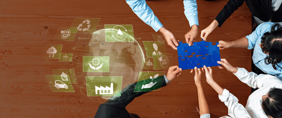 Obraz premium A diverse team collaborates over puzzle pieces, symbolizing commitment to sustainability with digital icons, highlighting eco-friendly practices and innovative solutions. Trope