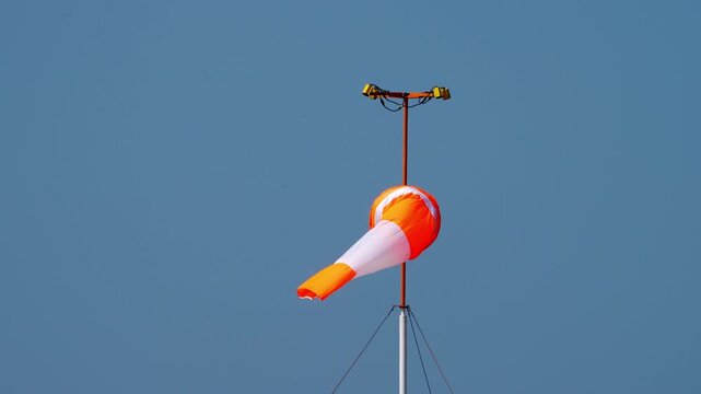 Orange and white windsock fluttering in the wind against a clear blue sky, showing wind direction and speed at airport.