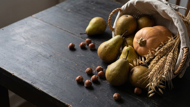 Autumn Harvest Basket with Pears, Pumpkin and Nuts on Dark Table