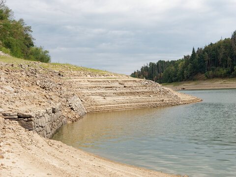 ORLIK RESERVOIR, CZECH REPUBLIC - AUGUST 7, 2026: Extremely low water levels at Orlik Dam, cracked muddy ground, green algae, and an old historic stone bridge normally submerged underwater.