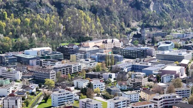 vaduz castle hilltop close orbit forested rocky outcrop town rooftops below cathedral spire liechtenstein capital push in drone footage elevated view heritage site travel destination scenic