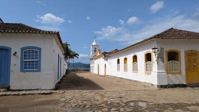 Paraty, Rio de janeiro: Wide angle scenic photograph of the historic colonial buildings and Capela de Nossa Senhora das Dores church tower on a sunny cobblestone street.