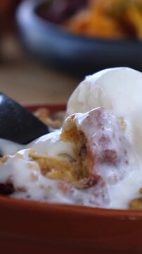 Dessert spoon lifts melting ice cream in rustic bowl, showing creamy scoop and crumb topping. Sweet dessert looks indulgent and close up in warm restaurant style plating. Spoon reveals soft texture.