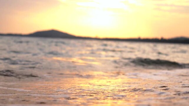 Waves roll onto wet sand at sunset, and golden surf glows across calm water. Coastal shoreline stays peaceful as foamy surf eases back under warm evening light, with foamline tracing shore.