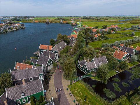 High angle wide horizontal aerial drone photograph of Zaanse Schans historic village, green wooden houses, windmills, river Zaan, canals, and polders in Zaandam, North Holland, Netherlands on day