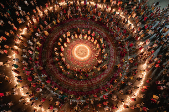  Aerial view of Garba dancers forming a mandala-like pattern around a central diya.
