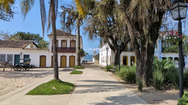  Slow motion cinematic view of a scenic pathway in the historic center near Rua da Capela, showing colonial architecture, ancient trees, and a horse carriage. Paraty, RJ, Brazil.