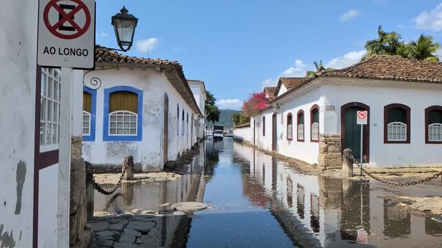 Paraty, Rio de janeiro: Slow motion static shot of a colonial street flooded by the high tide near the tourist port, showing beautiful architecture reflections on the water.