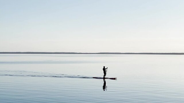Man Paddleboarding on Calm Lake with Peaceful Water Reflection
