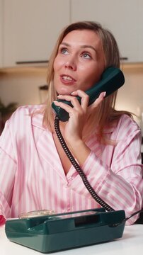 Adult woman at night home works as hotline operator uses retro corded phone listens with care. Caucasian girl at table on sofa at evening asks clarifying questions notes details finds solution fast