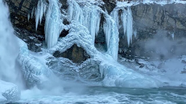 Frozen waterfall displays massive icicles along a rugged rocky cliff above chilly waters.