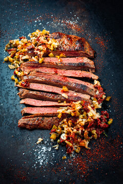 Barbecue roasted dry aged flank steak sliced with relish made of gherkin, onions and sun dried tomatos served as top view on a rustic plate