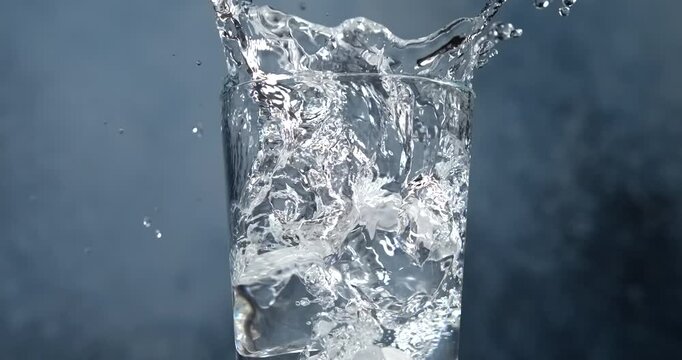 Ice cubes falling into a glass of water with splash in slow motion