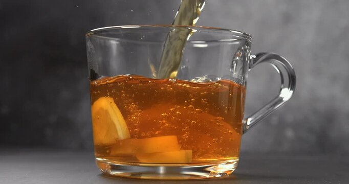 Hot tea pouring into glass cup with fresh lemon slices in slow motion