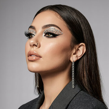 Glamorous woman with crystal eye makeup and rhinestones. High fashion beauty portrait with silver jewelry. Elegant female model with creative makeup.