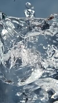 Ice cubes falling into a glass of water with splash in slow motion