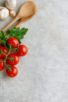 Fresh tomatoes, parsley, garlic and wooden spoons arranged along the edge of a light stone background with large copy space